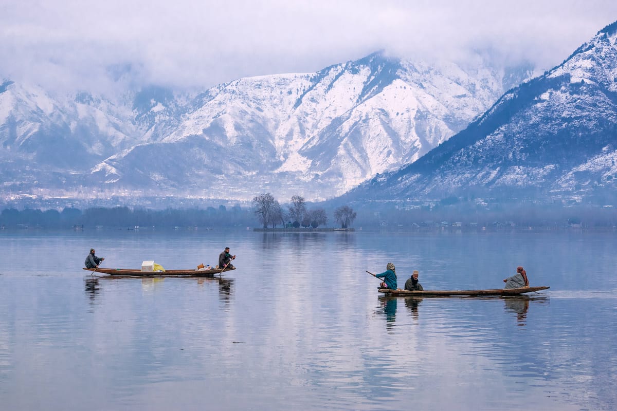 Shikaras crossing a mirror-still Dal Lake below snow-capped mountains, Srinagar